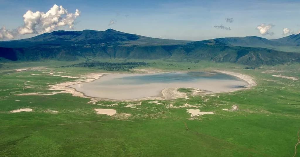 View from a crater rim across a green crater floor and its shallow lake