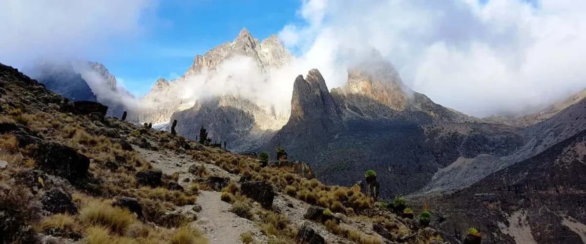 Mountain trail winding towards cloud-wrapped peaks